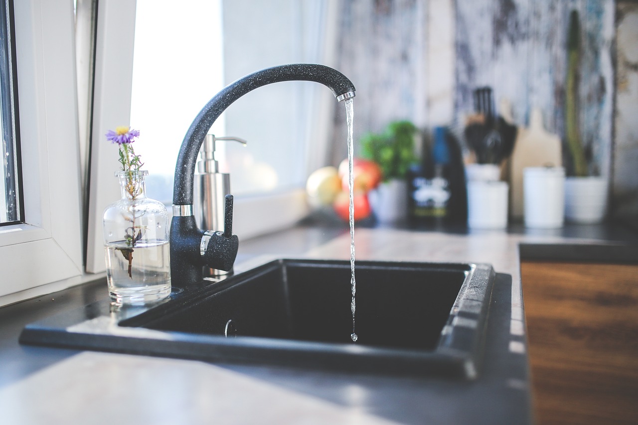 a black faucet with water dripping to show the pros and cons of soft water vs hard water